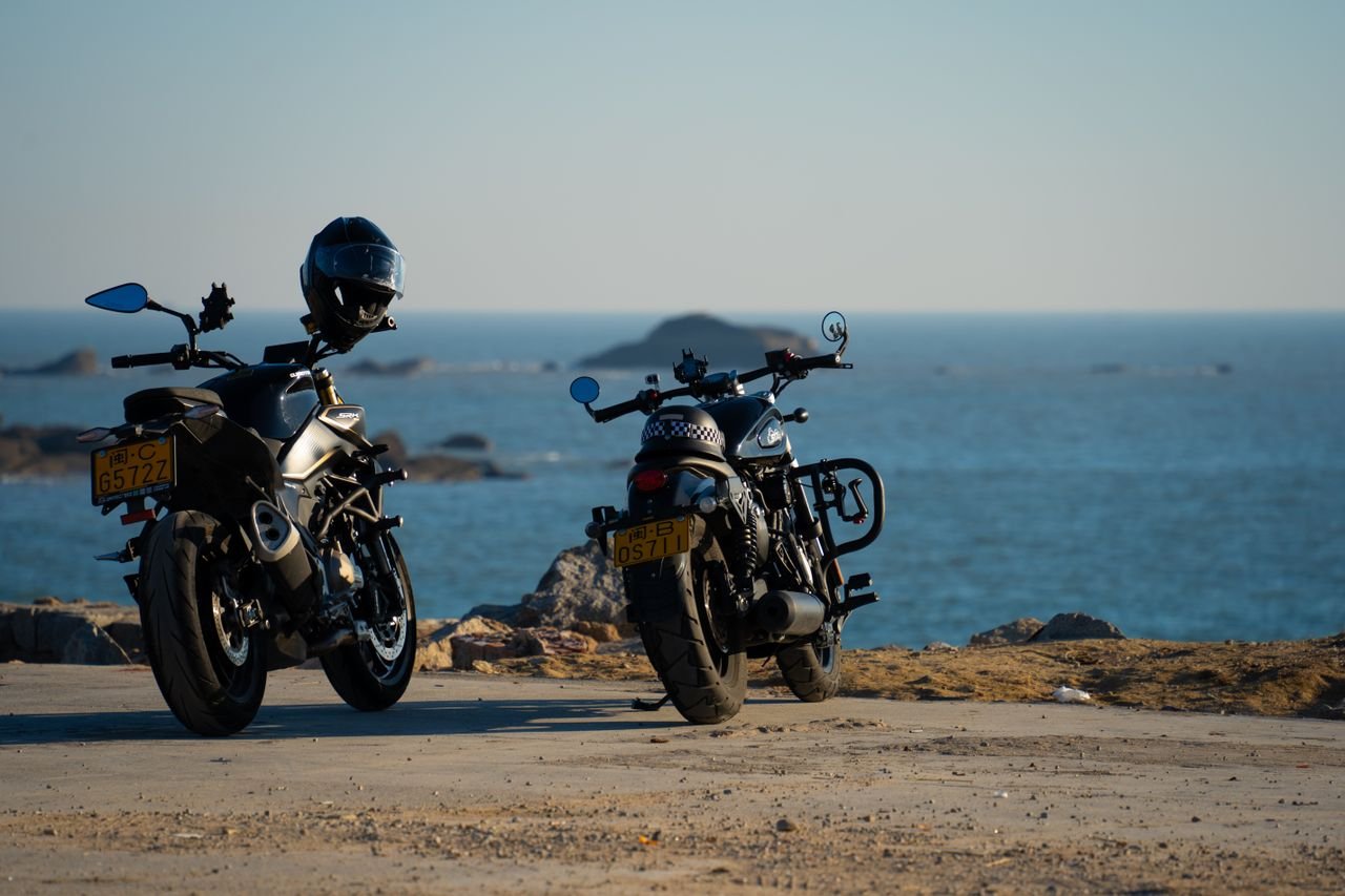 Home Two motorcycles parked by the ocean with a distant horizon and clear sky.