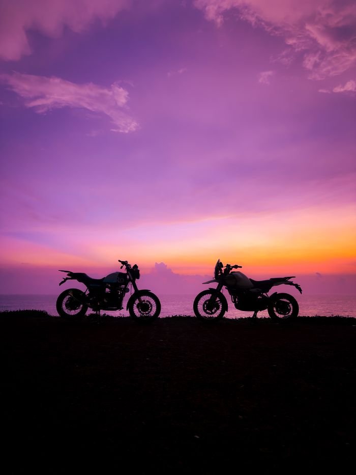 Two motorcycles silhouetted against a vibrant sunset sky in Varkala, Kerala, India.
